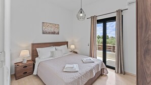 Un dormitorio con una cama, dos mesitas de noche con lámparas, una lámpara colgante, un cuadro en la pared y vistas al exterior a través de un ventanal corredero.