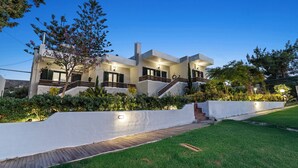 Una casa moderna de dos pisos con fachada blanca, varios balcones y un jardín cuidado.