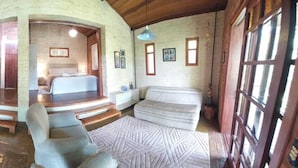 A rustic room with a fireplace, a bed, a sofa, and a staircase leading to an upper level. - Pousada Candeias Ltda (Cunha)