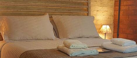 Una cama con cubrecolcha acolchada, almohadas y toallas dobladas.