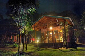 A wooden cabin with a glass front, surrounded by trees and a red vehicle parked outside. - Pousada Candeias Ltda (Cunha)