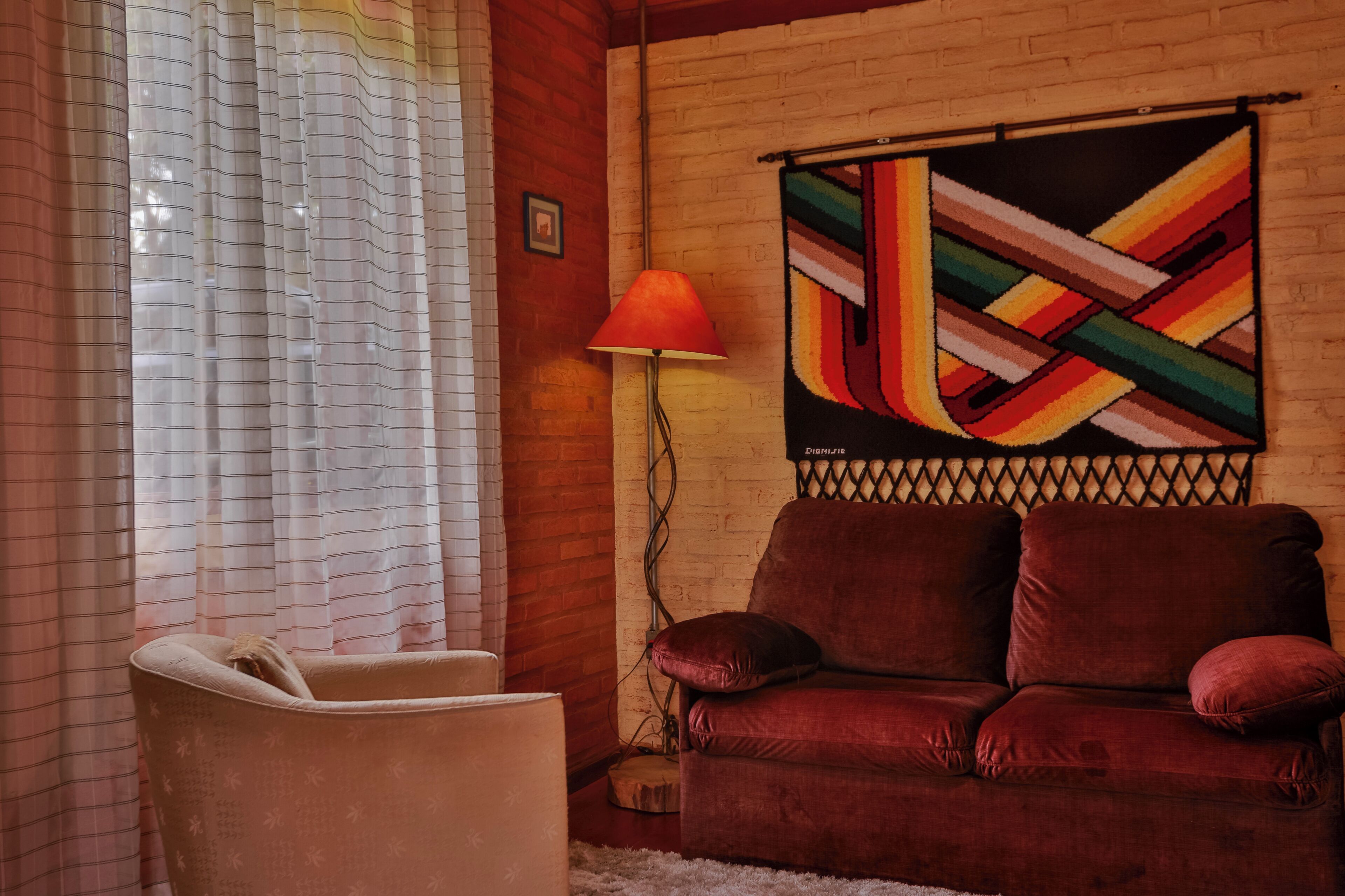A room with a red sofa, a white armchair, a patterned rug, and a colorful abstract painting on the wall.