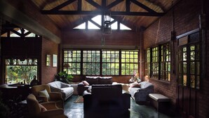 A spacious room with a high ceiling, large windows, and a variety of seating arrangements including sofas and chairs. - Pousada Candeias Ltda (Cunha)