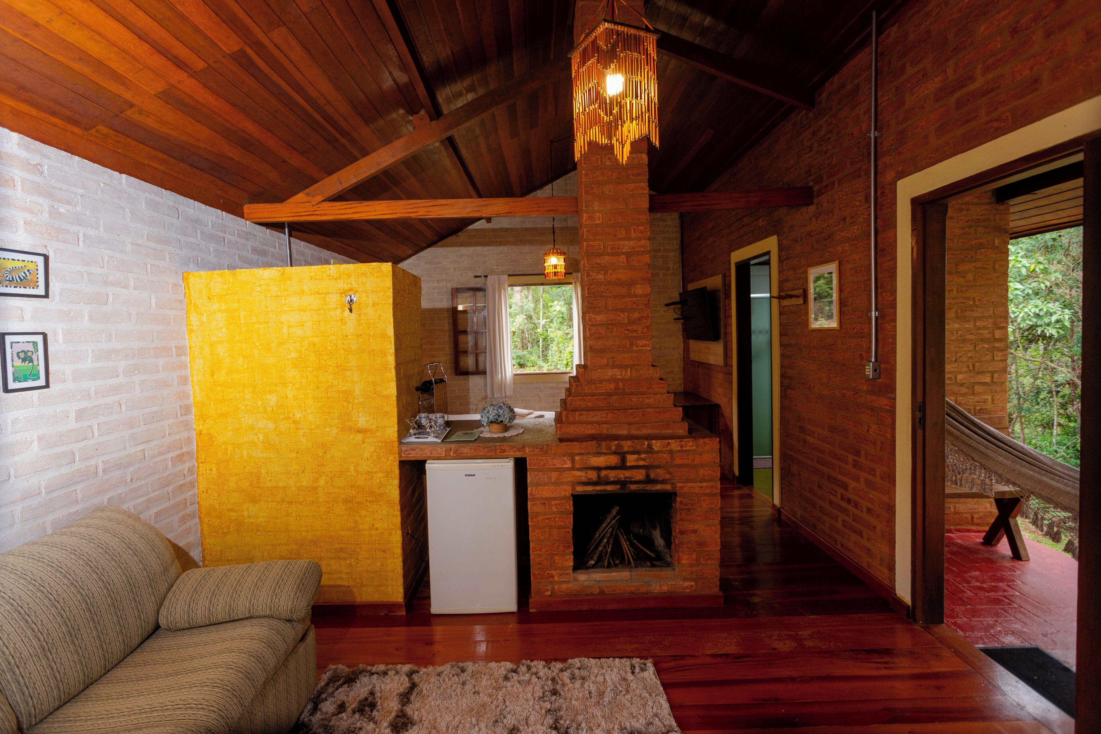 A rustic interior with a brick fireplace, wooden beams, a sofa, and a small kitchen area.