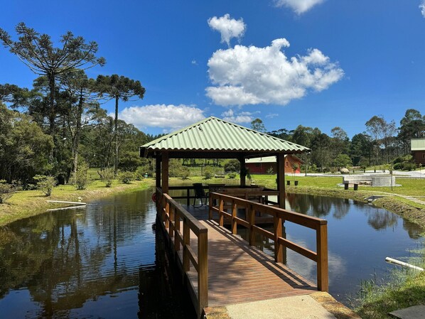 A wooden deck leading to a gazebo over a pond, surrounded by trees and a clear sky. - Vila Vert - Rancho Queimado - SC (Rancho Queimado)
