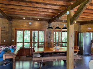 A wooden cabin interior with a dining area, a sofa, and a refrigerator. - Vila Vert - Rancho Queimado - SC (Rancho Queimado)
