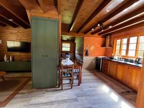 A wooden interior with a dining area, kitchen, and a TV mounted on the wall. - Vila Vert - Rancho Queimado - SC (Rancho Queimado)