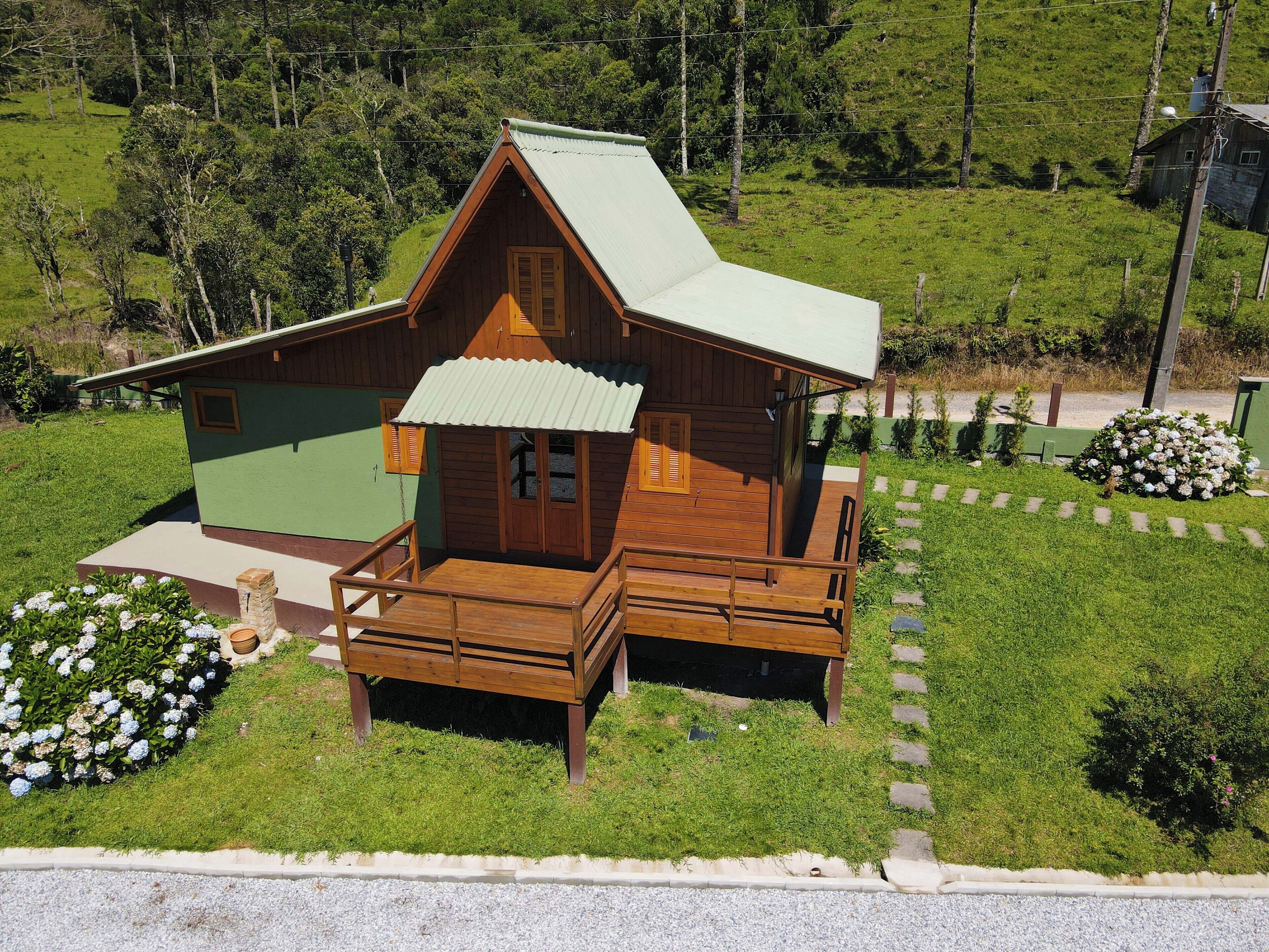 Una cabaña de madera con fachada verde, un balcón y un porche pequeño.