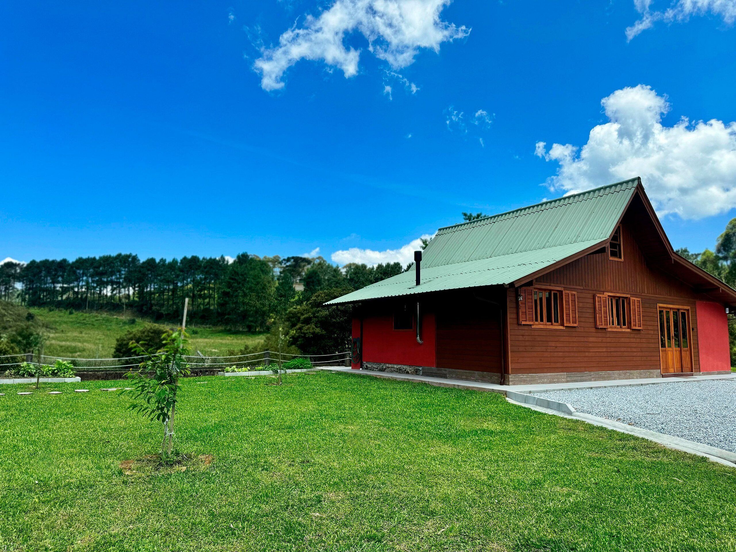 Une maison en bois rouge, avec un toit vert, entourée d’une pelouse bien entretenue et d’une allée gravillonnée.