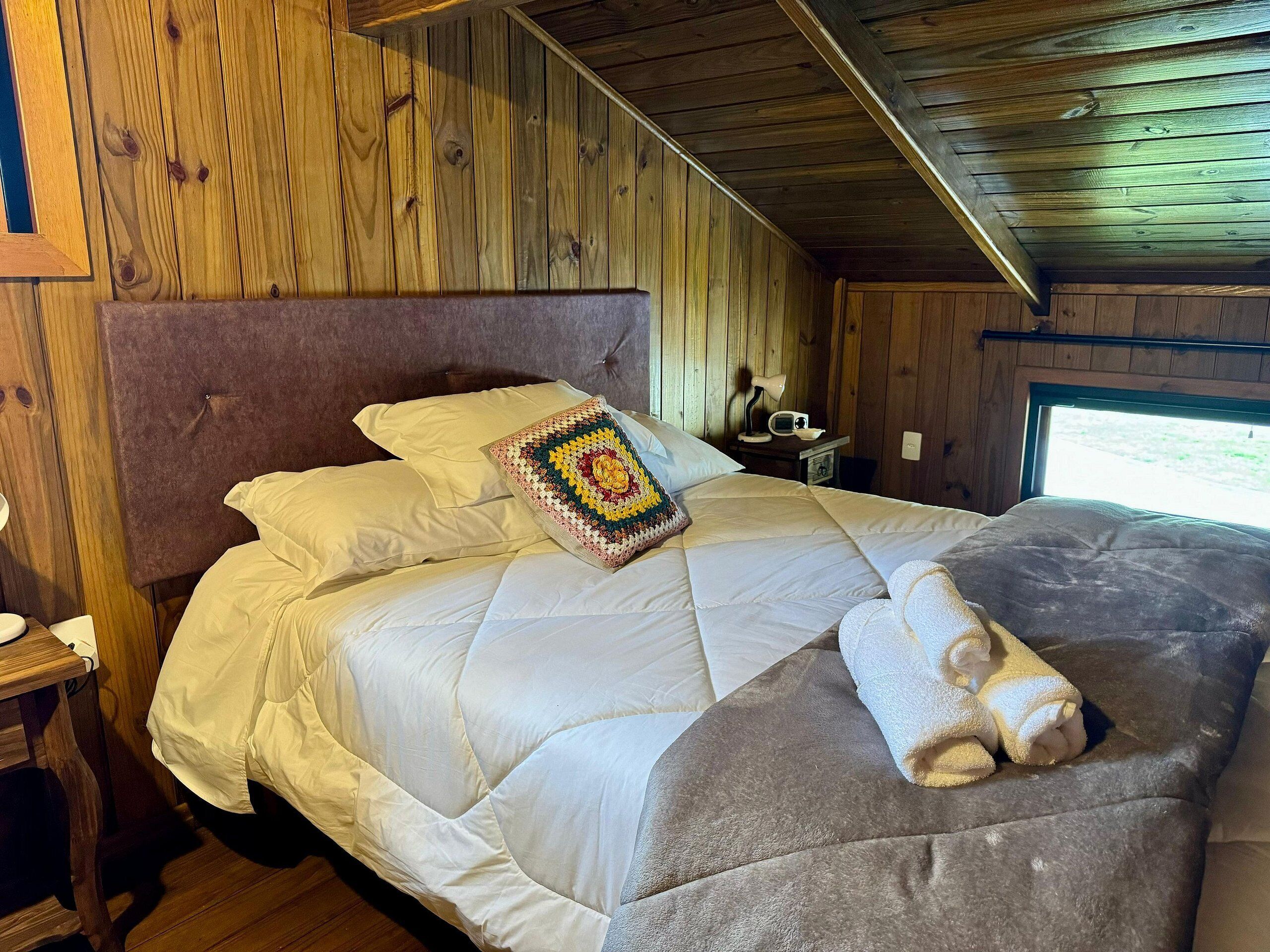 Ein Schlafzimmer in einer Holzhütte mit Bett, Kissen, einer Häkeldecke und einem Nachttisch mit Lampe und Radio.
