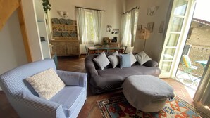 Ein Wohnzimmer mit einer Couch, einem Sessel, einem Couchtisch und einem Teppich. Im Hintergrund ist eine Essecke mit einem Tisch und Stühlen zu sehen.