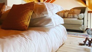 Ein Schlafzimmer mit Holzbalkendecke, einem Bett mit weißer Bettwäsche und einem Sofa mit gemusterten Kissen.