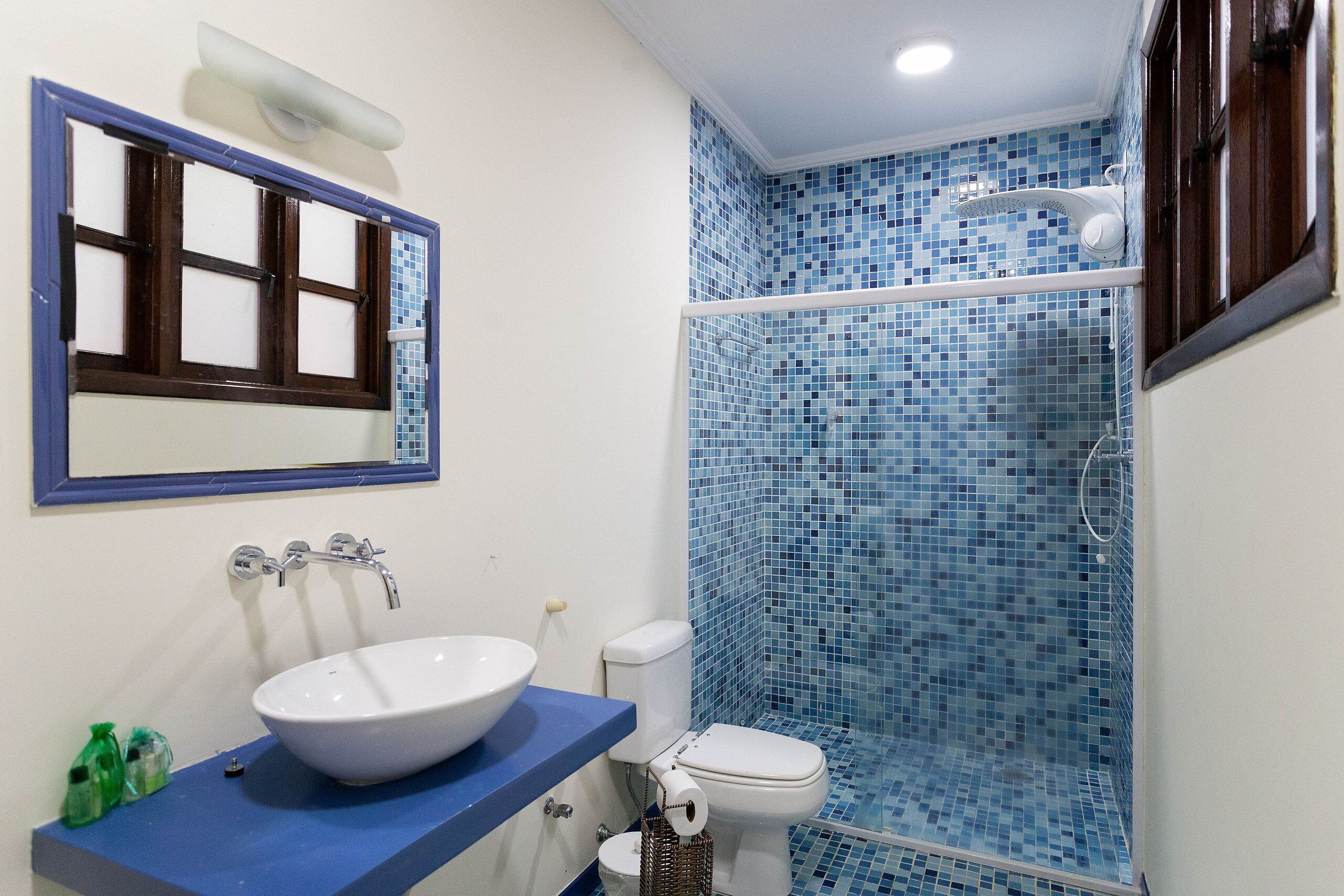 Ein Badezimmer mit Waschbecken in Weiß, einer blauen Duschkabine und einem Spiegel mit Holzrahmen.