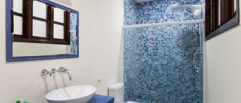 Un baño con lavamanos blanco, ducha con azulejos azules y espejo con marco de madera.