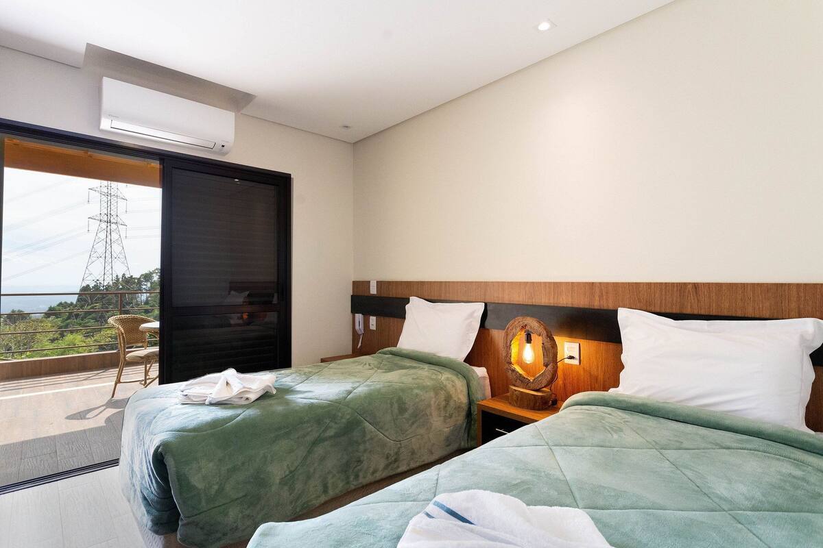Une chambre d’hôtel avec deux lits, une grande fenêtre donnant sur la ville, une tête de lit en bois et une table de chevet avec une lampe.