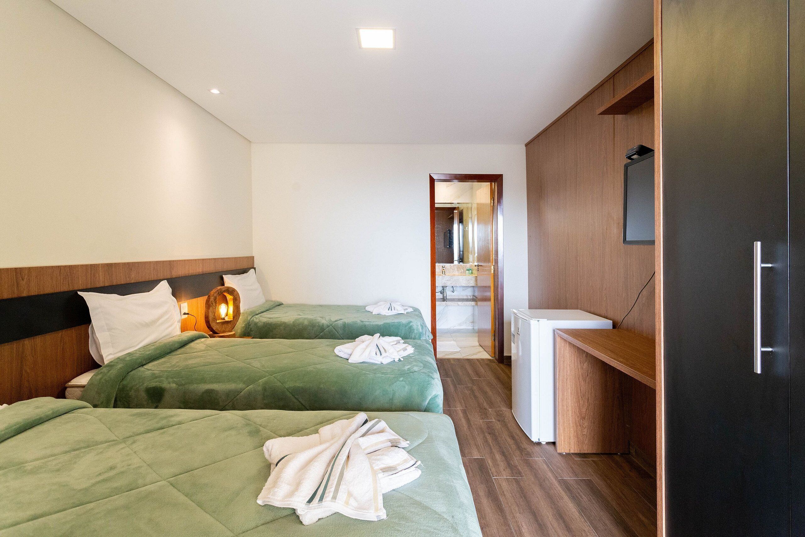 Une chambre d’hôtel avec deux lits, une tête de lit en bois, un petit bureau, un miroir et un réfrigérateur.