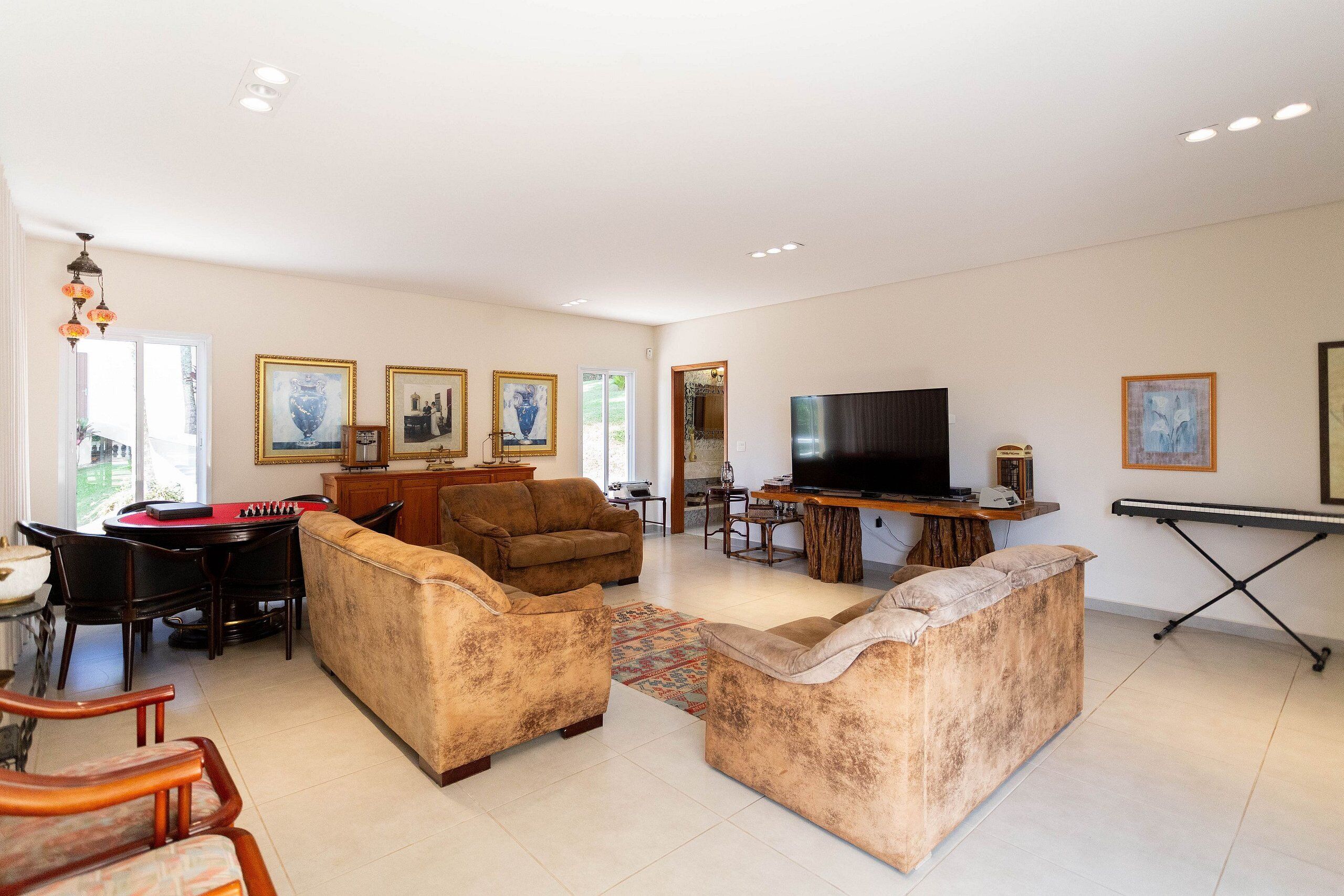 A spacious living room with a sofa set, a dining table with chairs, a television, and framed artwork on the walls.