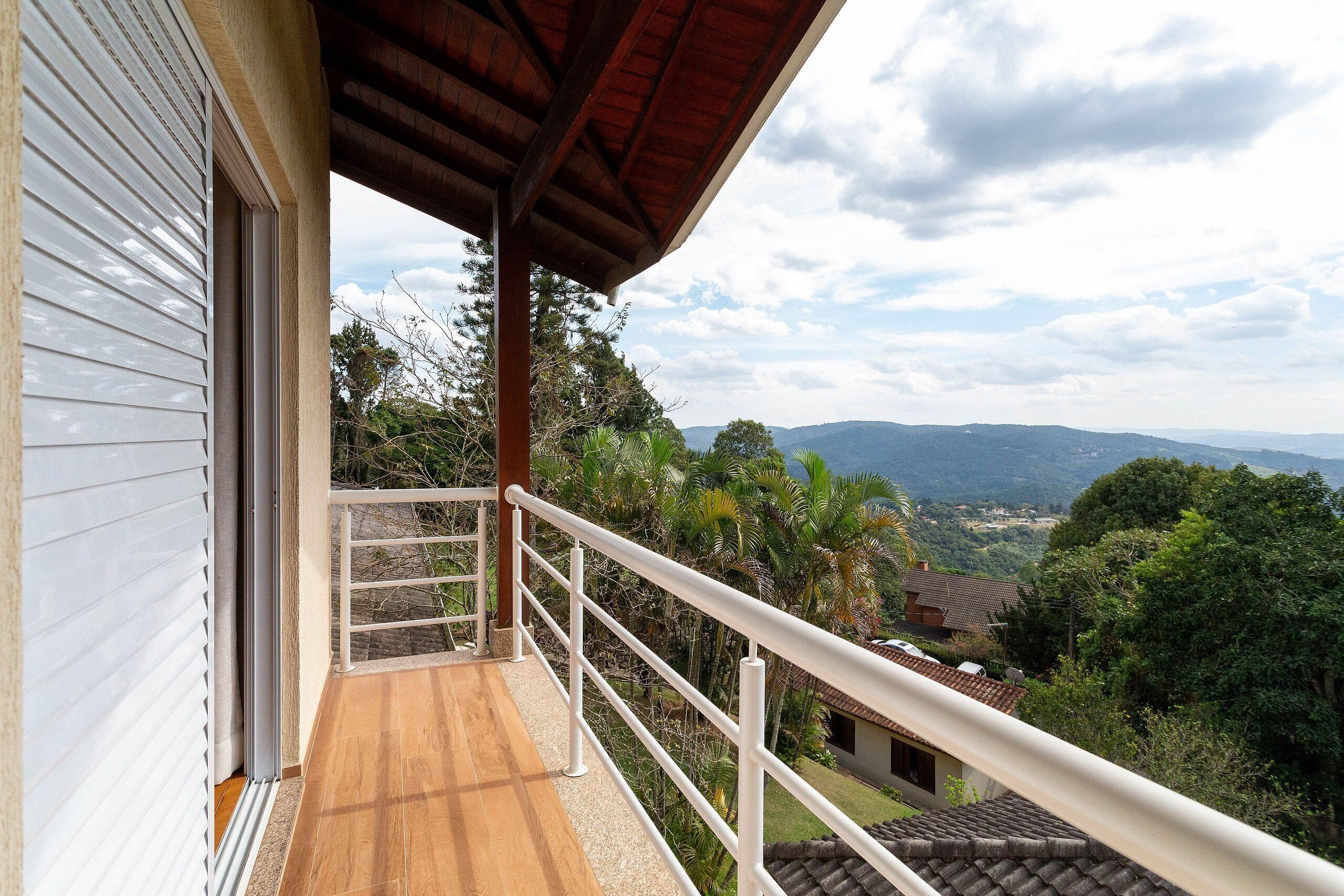 A balcony with a wooden floor, white railing, and a view of a mountainous landscape.