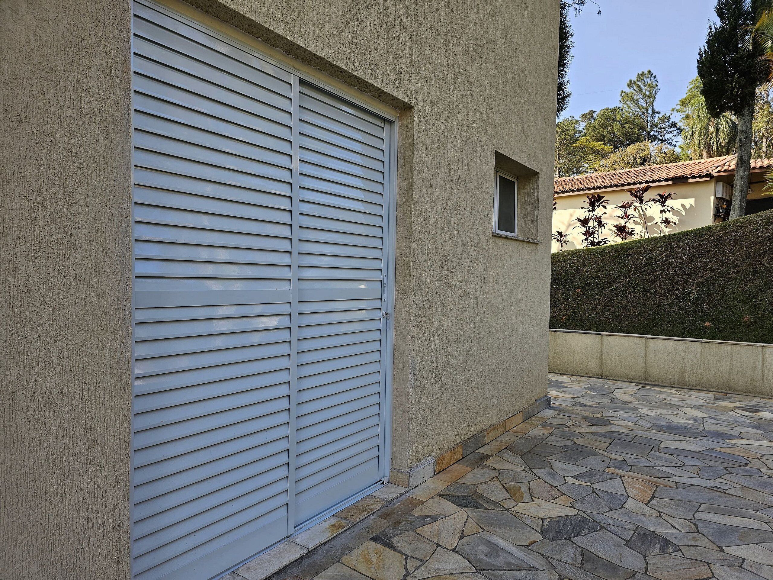 Un bâtiment avec une porte de garage fermée, une petite fenêtre et une terrasse dallée de pierres.