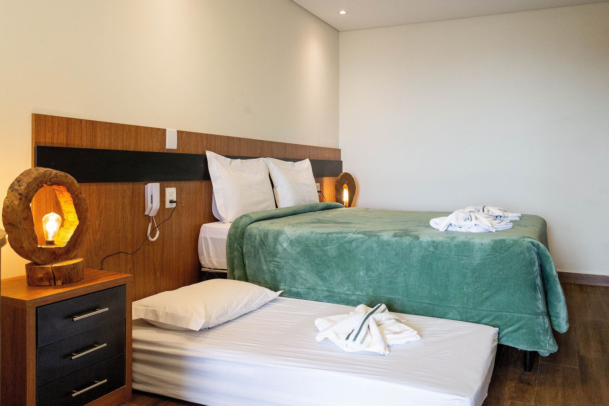 A hotel room with two beds, a wooden nightstand with drawers, a lamp, and a telephone.