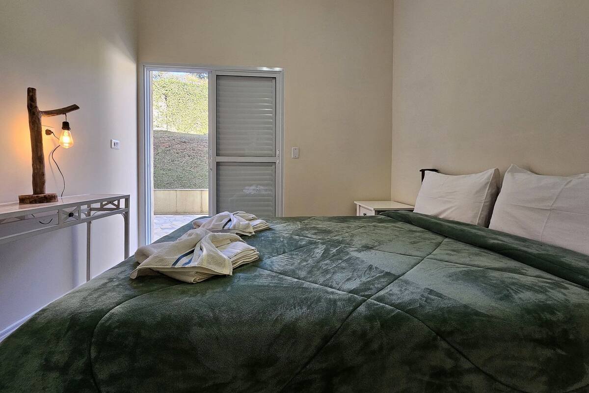 Une chambre à coucher avec un lit, une table de chevet, une lampe et une vue sur l’extérieur.