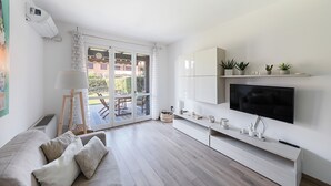 Ett modernt vardagsrum med en soffa, en tv och en balkong med utemöbler.