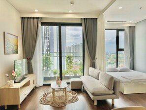 A modern hotel room with a sofa, a bed, a TV, and a balcony with a city view. - Vinhomes Smart City Luxury Apartment (Hanoi)
