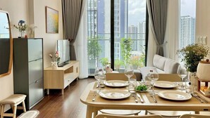 A modern dining area with a wooden table set for four, a sofa, and a TV in the background.