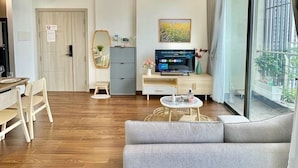 A modern living room with a grey sofa, wooden flooring, a television, and a large window with curtains.