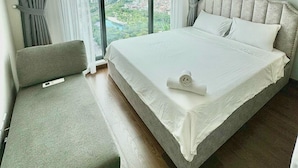 A modern hotel room with a large bed, a seating area, and a view of the cityscape through the windows.
