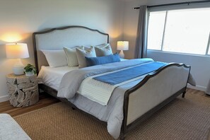 Un dormitorio con una cama, dos lámparas de noche, una mesita de noche con una planta y una ventana con cortinas.