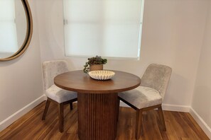 Une table de salle à manger ronde en bois, accompagnée de deux chaises rembourrées, d’une plante en pot et d’un bol décoratif posé sur la table.