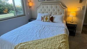 Une chambre avec un grand lit, un ventilateur de plafond, une fenêtre et des œuvres d’art encadrées accrochées au mur.