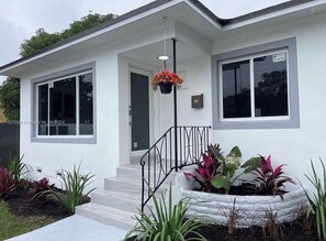A modern two-story house with a white exterior, a front door, and a small porch area with steps and a hanging planter. - CocoMango Villa Miami (North Miami)