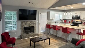 A modern kitchen with white cabinets, a stone fireplace, and a flat-screen TV mounted above it. - Charming Locust Grove GetAwayHome 4bd/3bath (Locust Grove)