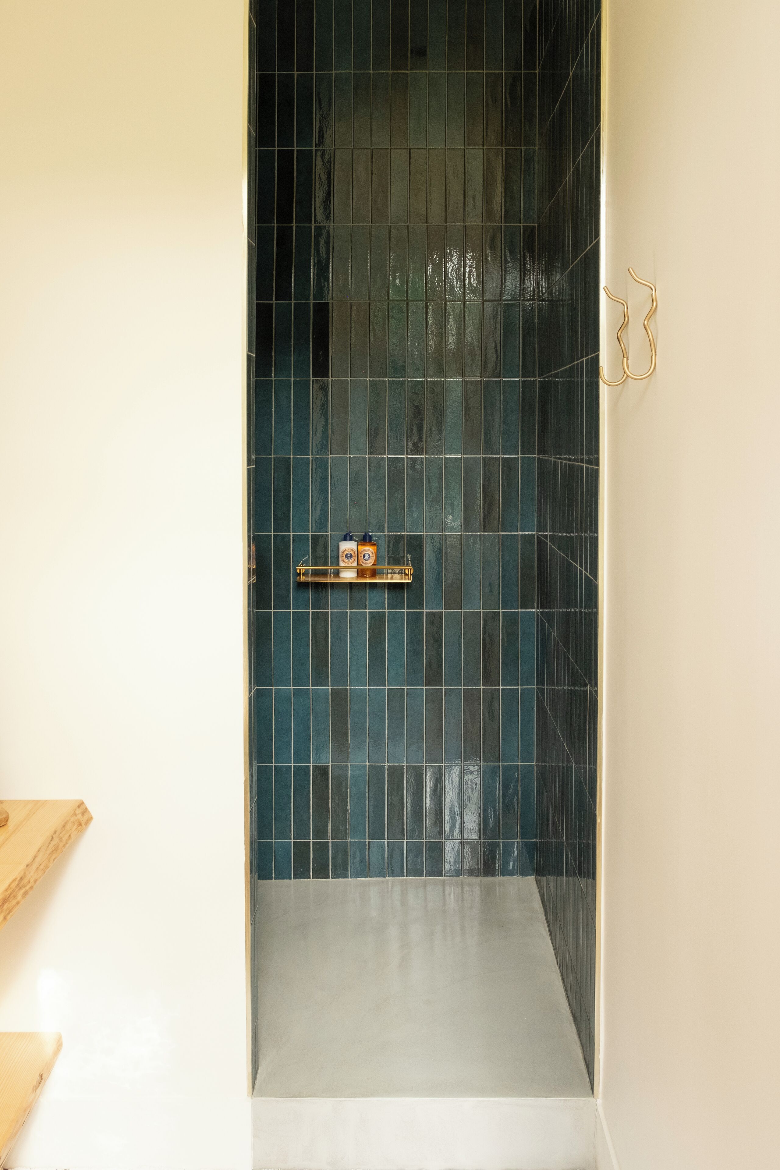 Un petit espace de douche, carrelé, avec une étagère où sont rangés les produits de toilette.
