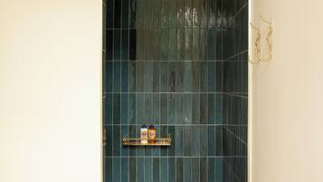 Un petit espace de douche, carrelé, avec une étagère où sont rangés les produits de toilette.