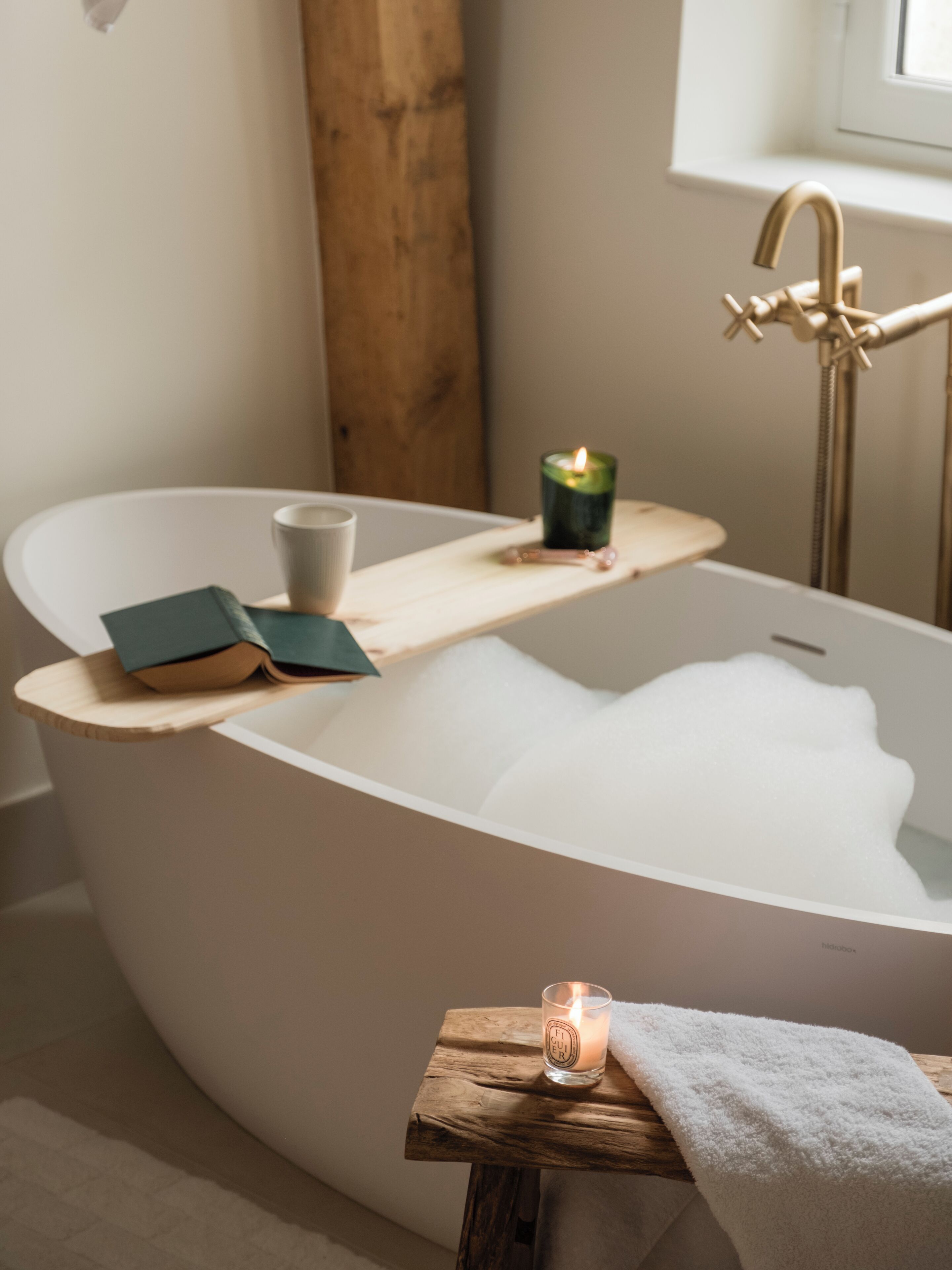 A modern bathroom with a freestanding bathtub, a wooden shelf with a candle, and a towel.