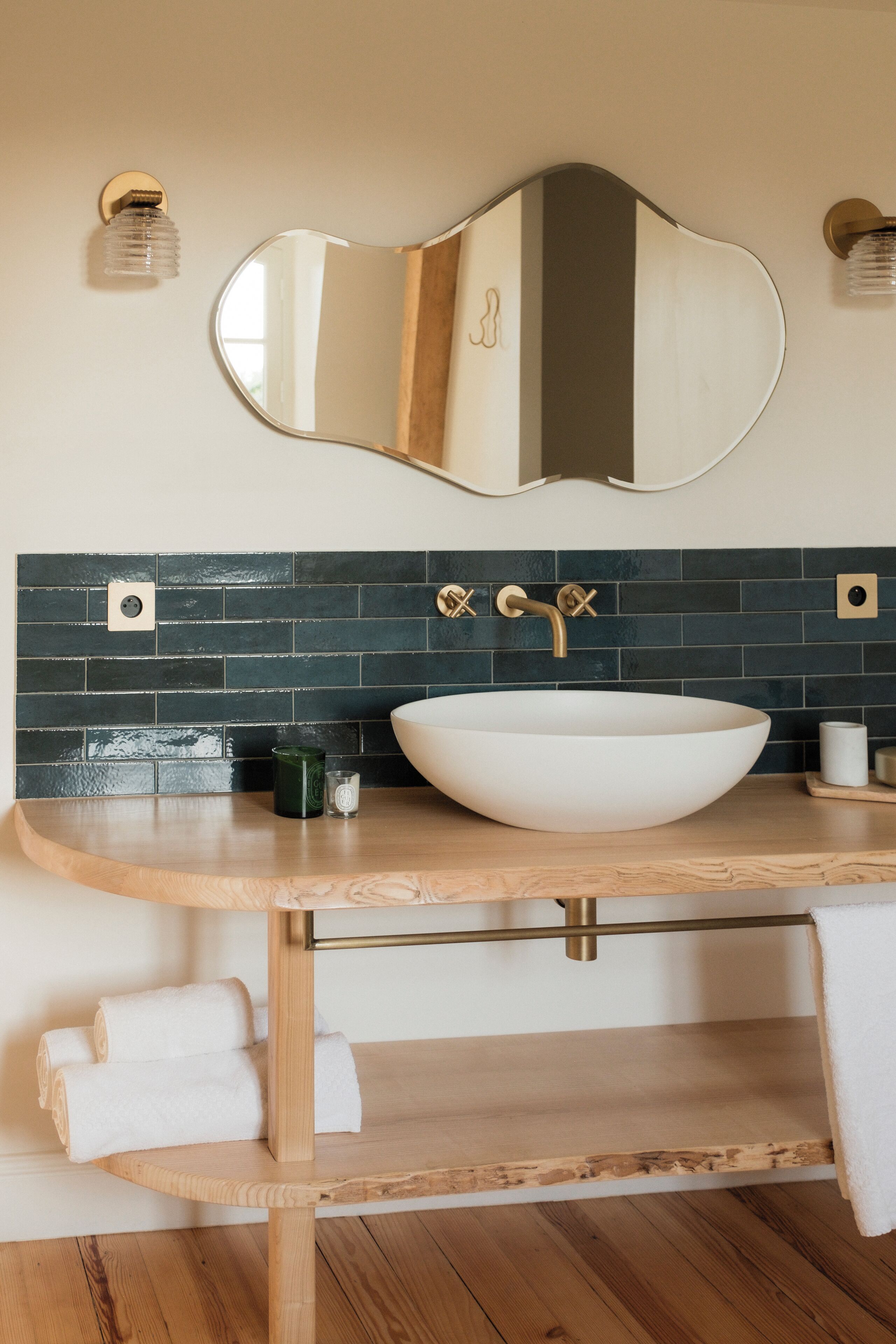 A bathroom with a white vessel sink, a wooden vanity, a large mirror, and a dark tiled backsplash.