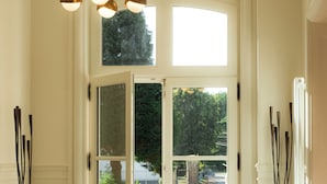 Un vestíbulo con una puerta doble que da al exterior, una lámpara de pie de cobre y un candelabro moderno.