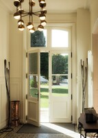 Un vestíbulo con una puerta doble que da al exterior, una lámpara de pie de cobre y un candelabro moderno.