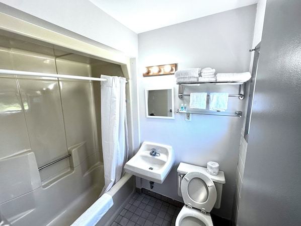 A bathroom with a bathtub, a sink, a toilet, and a mirror. - Budget Host Inn Manistique (Manistique)