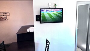 Una habitación con una televisión de pantalla plana en la pared, una mesita con una silla y una puerta a la derecha.