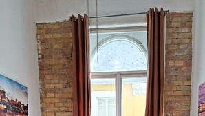 A bedroom with a large bed, a window with curtains, brick walls, and two bedside tables with lamps. - GoodMo Budapest Smart Rooms (Budapest)