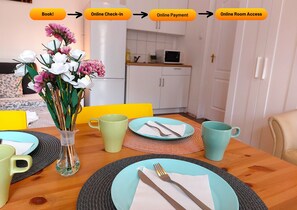 Un comedor con una mesa de madera dispuesta para dos personas, que incluye un jarrón de flores, dos platos con cubiertos y dos tazas.