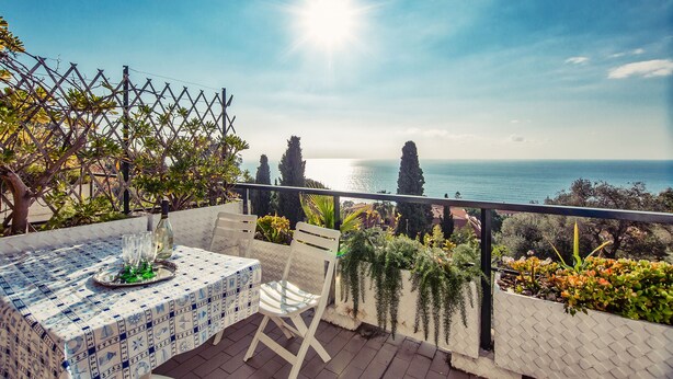 A terrace with a table set for two, overlooking a coastal view.