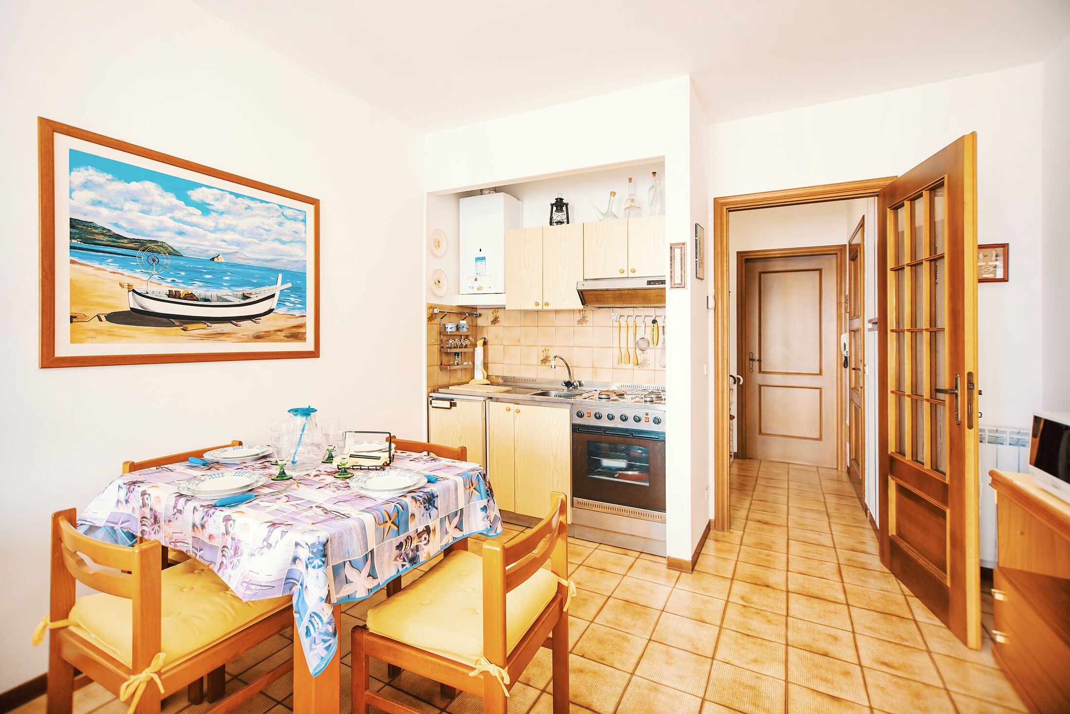 A kitchen with a dining table, chairs, and a painting of a boat on the wall.
