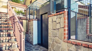 A narrow stone staircase leading to a door, a metal railing, and a stone wall with a window.