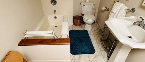 Un baño con bañera, inodoro, lavabo y un barril de madera.