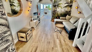Amplia sala de estar con suelo de madera, un sofá, una mesita redonda y un espejo decorativo.